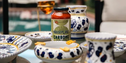 Pot de sauce Carbone sur table avec vaisselle ornée de motifs colorés.
