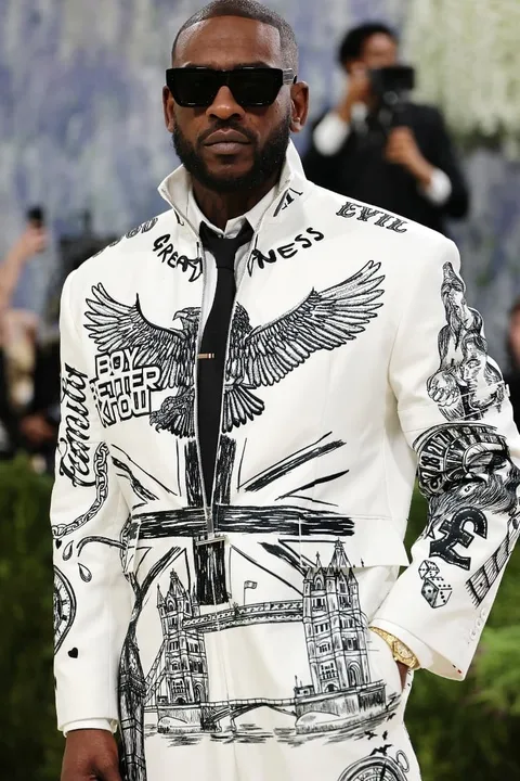 Homme en veste blanche avec motifs noirs artistiques, lunettes de soleil.