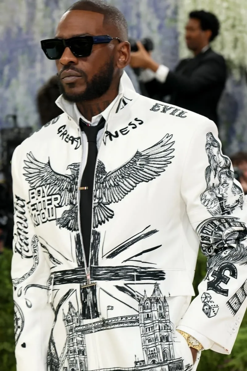 Homme en costume blanc avec motifs noirs et lunettes noires.