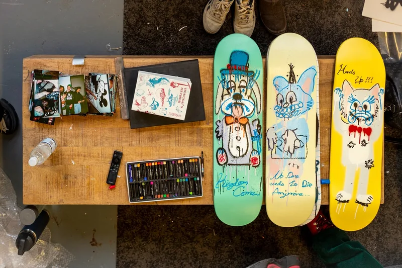 Trois planches de skate peintes à la main sur une table avec des photos et des crayons.