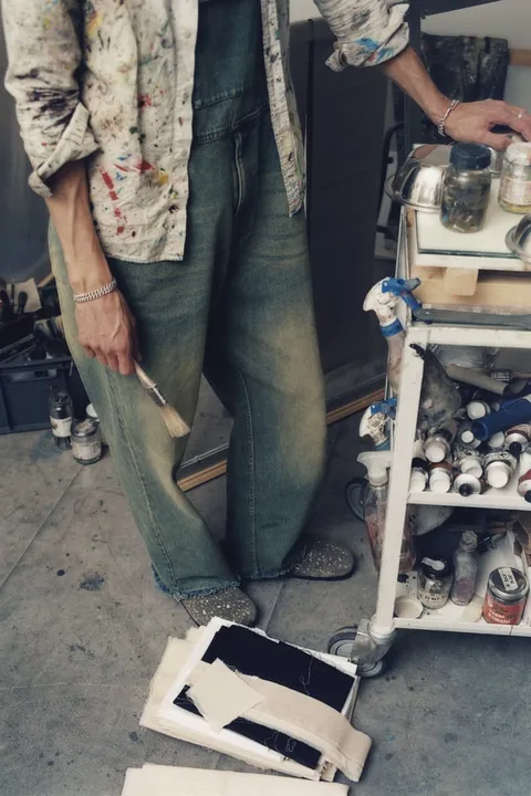 Personne tenant un pinceau dans un atelier d'art avec des toiles et des fournitures.