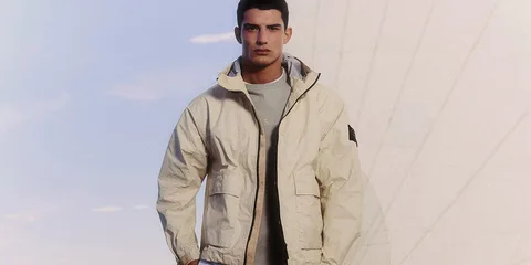 Homme en veste beige devant un ciel bleu et structure moderne.