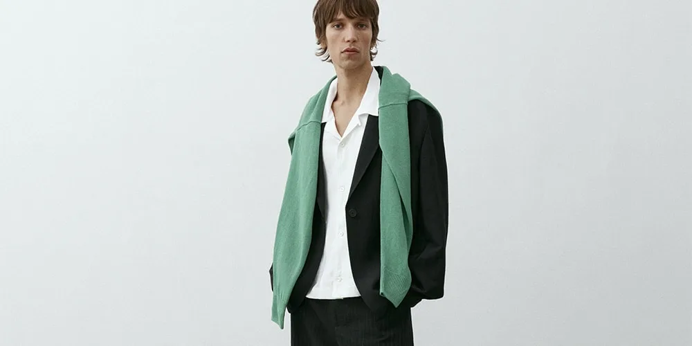 Personne en costume noir avec chemise blanche et pull vert sur les épaules.
