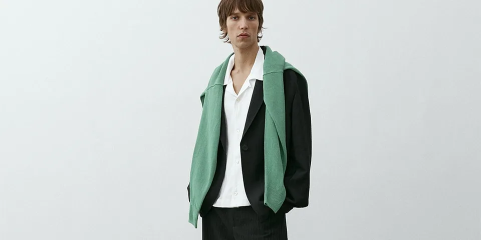 Personne en costume noir avec chemise blanche et pull vert sur les épaules.