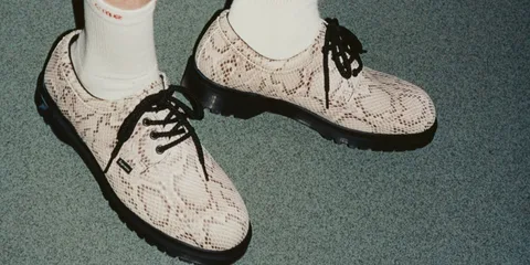 Chaussures à motif serpent avec lacets noirs sur sol vert.