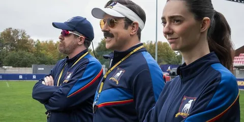 Trois entraîneurs en tenue d'équipe sur le terrain de football