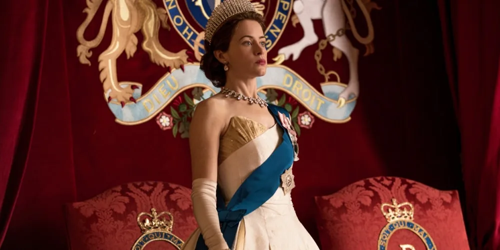 Femme en robe royale avec diadème devant un emblème sur un fond rouge.