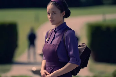 Jeune femme en robe violette avec sac à dos, regardant au loin.