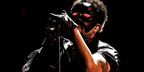 Chanteur masqué sur scène en lumière tamisée.