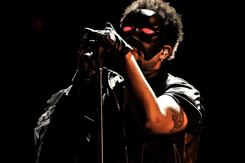 Chanteur masqué avec micro sur scène, ambiance sombre.
