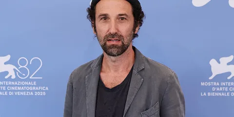 Homme avec barbe, chapeau noir, fond bleu à un événement de cinéma.