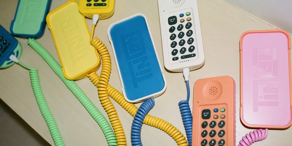 Téléphones colorés rétro sur une surface beige, câbles spiralés assortis.