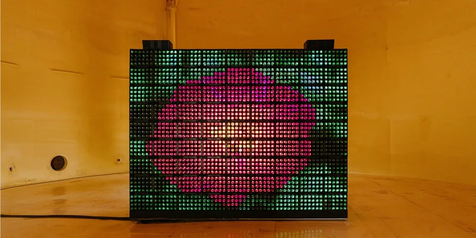 Installation lumineuse colorée en forme de fleur dans environnement orange.