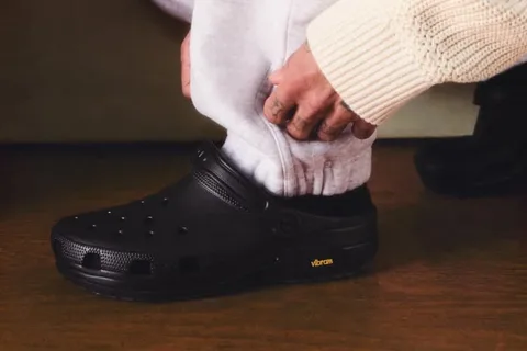 Personne portant des Crocs noires avec semelles Vibram sur un sol en bois.