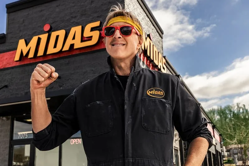 Homme en tenue de travail devant un magasin Midas.
