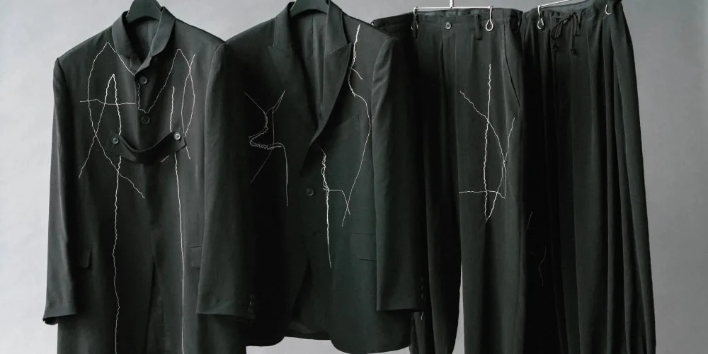 Costumes noirs avec motifs de couture blanche sur cintres.