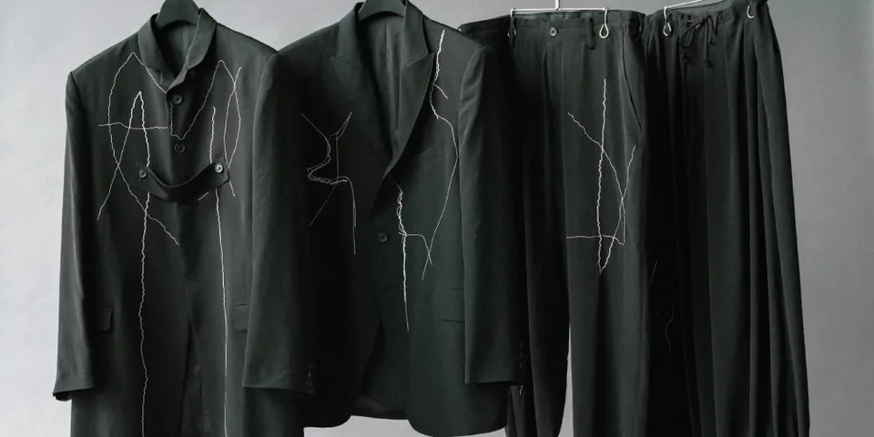 Costumes noirs avec motifs de couture blanche sur cintres.