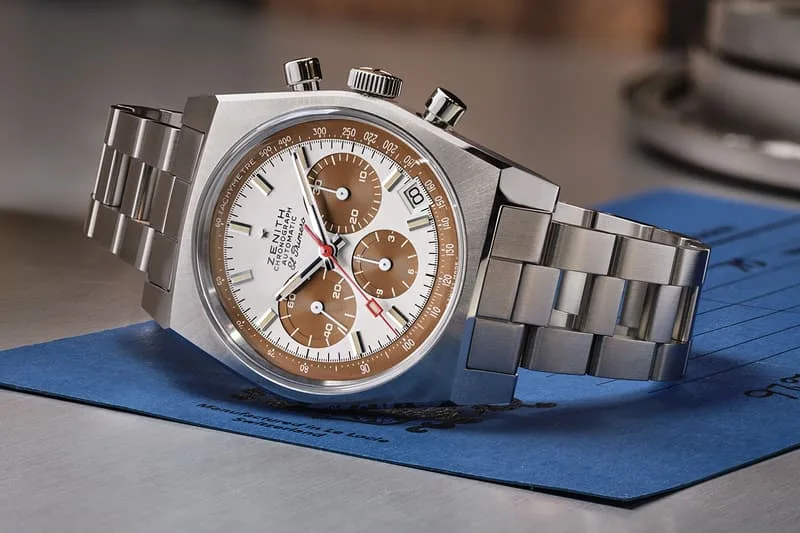 Montre-bracelet en acier avec cadran blanc et marron sur surface métallique.