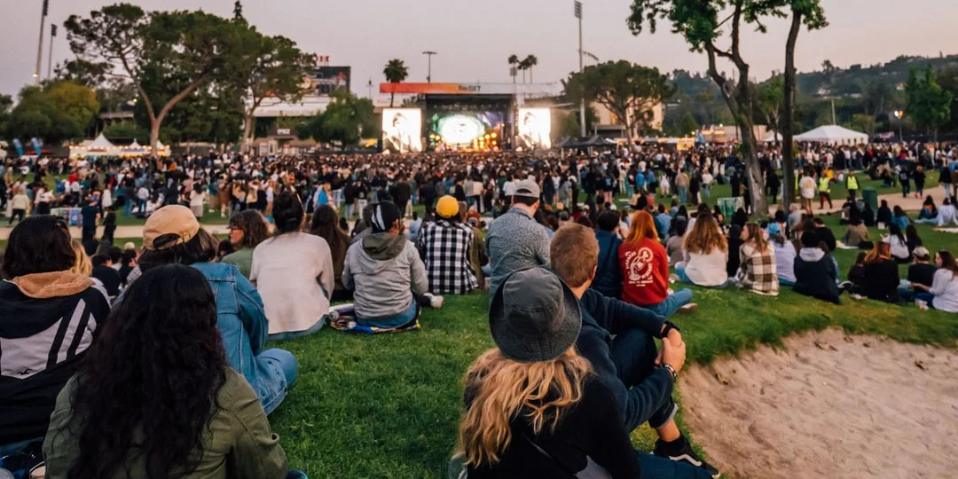 Foule assise et debout, regardant un concert en plein air.